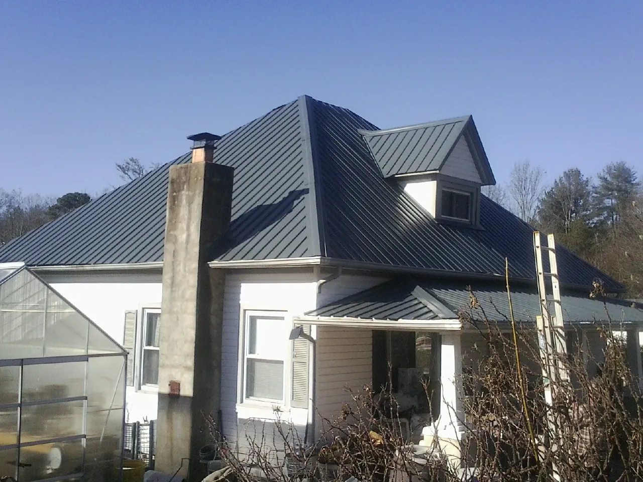 Dark blue standing seam metal roof on a white farmhouse with dormer — Slate & Tile Roof Repair by Roofing Brothers in Eagle Creek