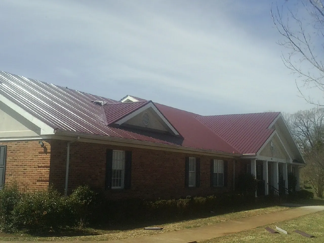 Red metal roof with gabled entries on a long brick building, from a Hail Damage Roof Repair job in Eagle Creek