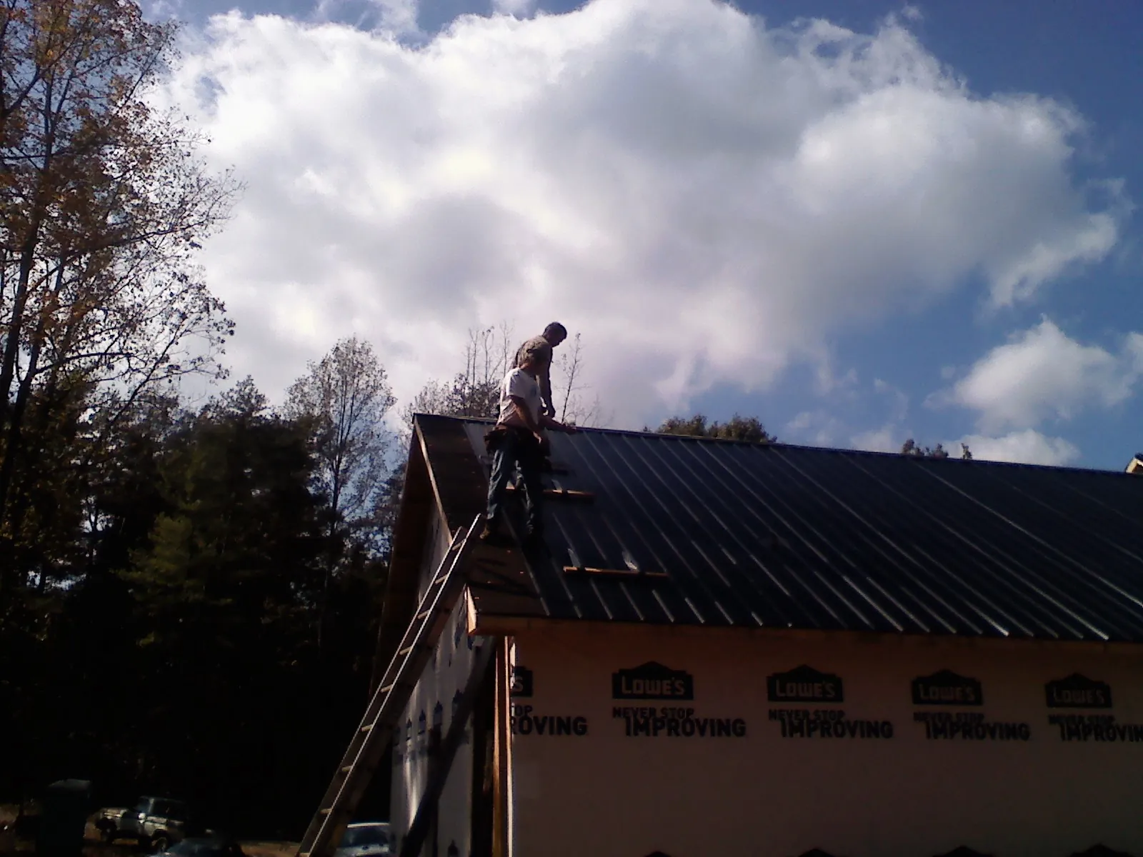 Roofer fastening dark metal panels high against a cloudy sky, from a Roof Inspection job in Eagle Creek