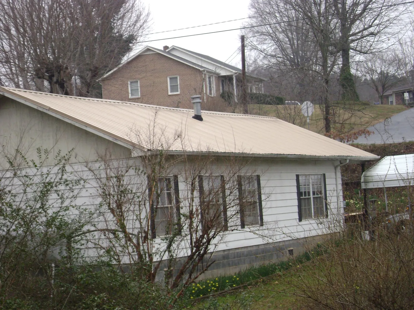 Tan metal roof on a white sided house set into a hillside — Commercial Roofing by Roofing Brothers in Eagle Creek